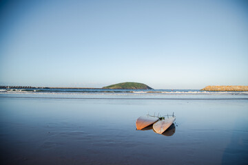 Two surfboards on the beach at sunset with Muttonbird Island in the distance. Coffs Harbour, Australia
