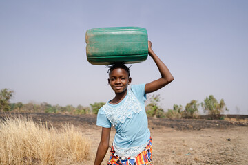 Brave young African girl on her long and arduous walk home from the distant village well, wasting...
