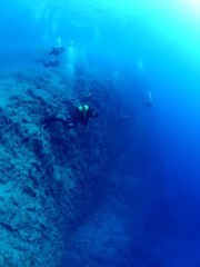 Fototapeta na wymiar scuba divers around a reef underwater deep blue water big rocks 