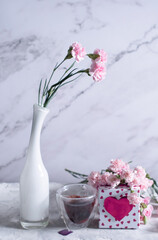 pink carnations in a white vase and coffee cups in a heart-shaped pink box,