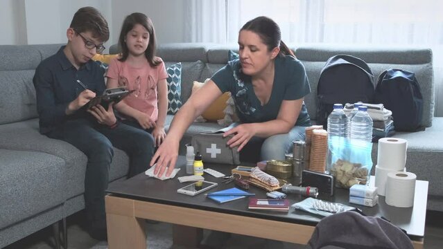 Mother preparing emergency backpack with her children in the living room