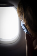 Detail photo with coronavirus mask covering passenger face looking through a window inside airplane