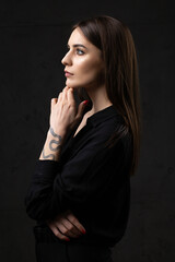 Portrait of a young brunette with long hair in the studio. Dramatic photo in dark colors. A girl with a snake tattoo on her arm.