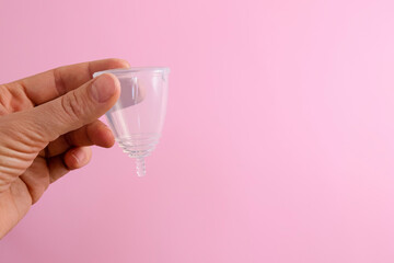 Hand holding silicone menstrual cup on pink background with copy space