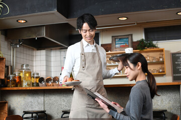 飲食店（レストラン）で働くエプロン姿のアジア人の男性と女性客