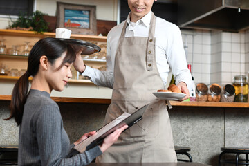 飲食店（レストラン）で働くエプロン姿のアジア人の男性と女性客