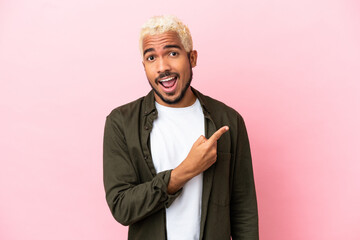 Fototapeta premium Young Colombian handsome man isolated on pink background surprised and pointing side