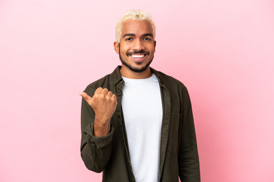 Young Colombian handsome man isolated on pink background pointing to the side to present a product