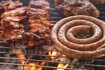 A South African braai. Beef boerewors with lamb chops and chicken kebabs or espetadas on grill with flaming hit coals in the background. Traditional social gathering