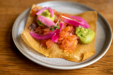 Mexican food, fried corn tortilla with smoked salmon, guacamole sauce and pink pickled onions