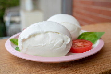White ball of Italian soft cheese Mozzarella di Bufala Campana with fresh green basil and red tomato