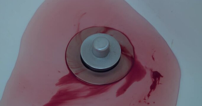 Close-up of blood and water washing down a shower drain.