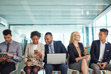 What a friendly environment to work in. Shot of a group of focussed young businesspeople seated together on chairs and making notes using different methods while waiting in the office during the day.