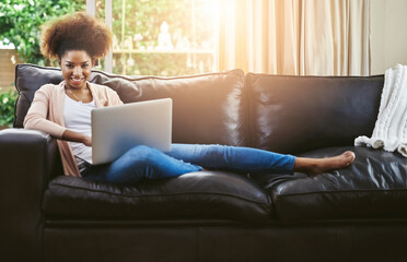 Naklejka premium Its my lazy day online. Portrait of an attractive young woman using laptop while chilling at home on the sofa.
