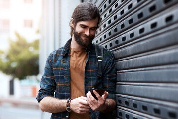 Connecting you through every walk of life. Shot of a handsome young man using his cellphone while walking in the city.