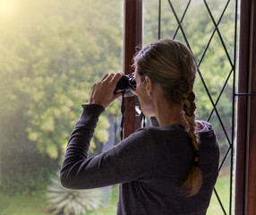 woman looking out of window with binoculars