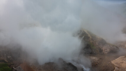 A geyser erupts on the mountainside. There are drops of hot water in the air, clouds of thick steam. Poor visibility. Kamchatka. Valley of Geysers