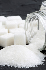 Glass jar with sugar black background.Diabetes. Scattered white sugar on a black table. Copy space....