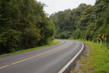 Beautiful road and arrow danger curve road sign warning on forest mountain background....