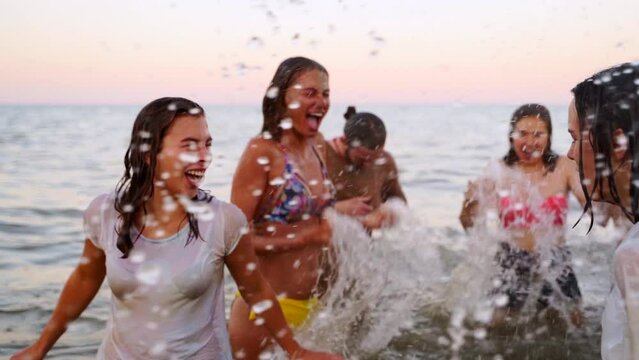 Joyful people have fun splashing water in sea. Girl dives giving salute. Friends celebrate Holi festival of colors, love, unity. End of lockdown, covid pandemic isolation.