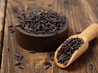 pile of black rice in a wooden bowl on a wooden table close-up