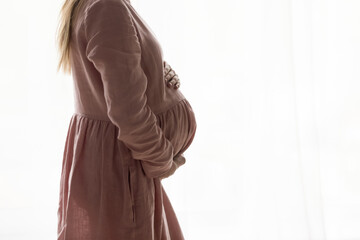 Cropped side view young pregnant woman holding in arms big belly on white background, feeling inspired waiting for baby, enjoying third trimester pregnancy period, copy space for IVF advertisement.