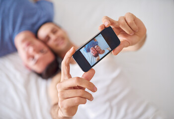 Capturing a moment of love. Shot of a young gay couple taking a selfie while relaxing in bed.
