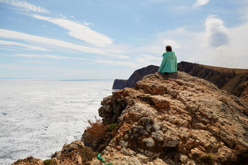 Lake Baikal in spring, the time of the ice drift. A woman sits on a rock and enjoys a beautiful...