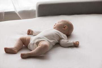 Peaceful carefree adorable little newborn baby boy girl in bodysuit sleeping on folded couch. Full...