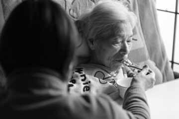 食事を介助してもらって食べる高齢女性　在宅介護　老人介護
