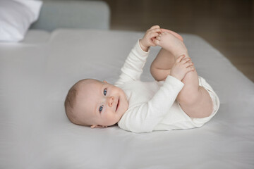 Portrait of happy sincere cute few months baby boy girl holding tiny feet in hands, lying alone on...