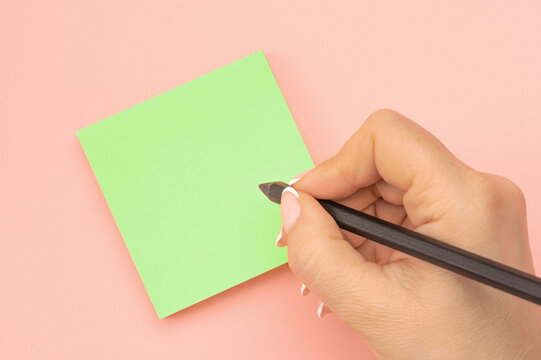 Hand written notes black pencil on green sticker. pink table background. Mockup sticky Note Paper. empty sheet for notes on pink bulletin board