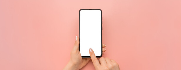Hand holding cellphone device and touching screen on pink background. Isolated hands and smartphone on pink background. Female hand holding modern black cell phone in vertical position