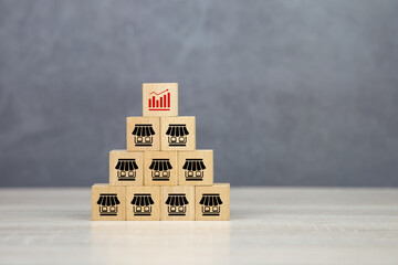 Close-up wooden block stack pyramid with graph and franchise business store icon for franchising to growth branch expansion and business banking loans. - obrazy, fototapety, plakaty