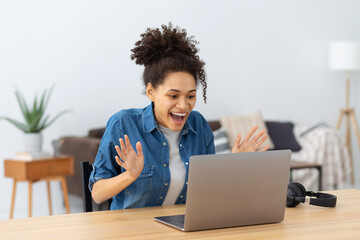 Portrait of excited young African American woman celebrating success while sitting with laptop at...
