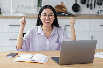 Portrait of excited Asian student woman reading test results celebration success sitting with laptop at home. Happy female freelancer working and having good news, she receive payment