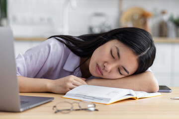 Close up portrait of tired Asian woman freelancer or student sleeping at the workplace at home....