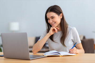 Distance learning, online education. Portrait of beautiful caucasian woman freelancer or student using laptop computer taking notes, watching training courses working from home or modern office