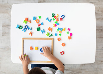 Foreign language classes. Top view of kid making ABC note with colorful English letters, top view,...