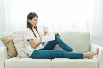Fototapeta premium ソファに座る中高年女性（飲み物、読書） 