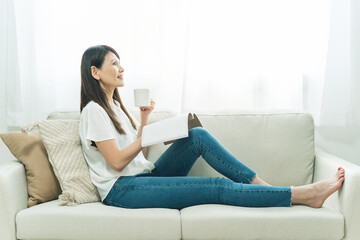 Obraz premium ソファに座る中高年女性（飲み物、読書） 