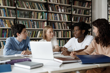 African student guy with schoolmates sit at table in library discuss collaborative task. Multi ethnic schoolgirls schoolboys learn subject, studying together, gain knowledge, prepare for exams concept