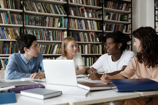 African student guy with schoolmates sit at table in library discuss collaborative task. Multi ethnic schoolgirls schoolboys learn subject, studying together, gain knowledge, prepare for exams concept