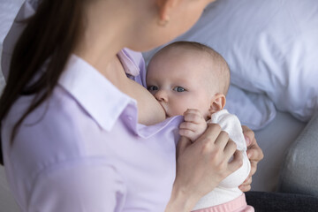 Close up adorable little newborn baby boy girl sucking milk from breast of caring mother, getting...