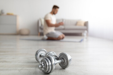 Millennial Arab guy exercising at home during covid lockdown, selective focus on dumbbells