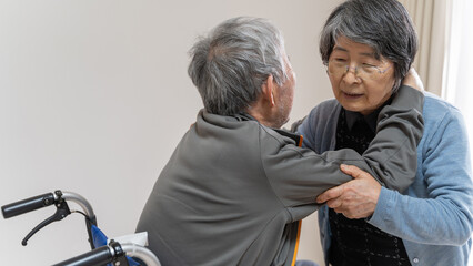 介護が必要な高齢の夫を車椅子から立ち上がらせる老人の妻