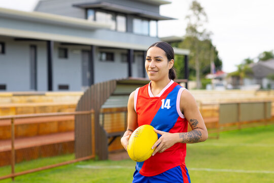 one female footy player holding aussie rules football outside club rooms