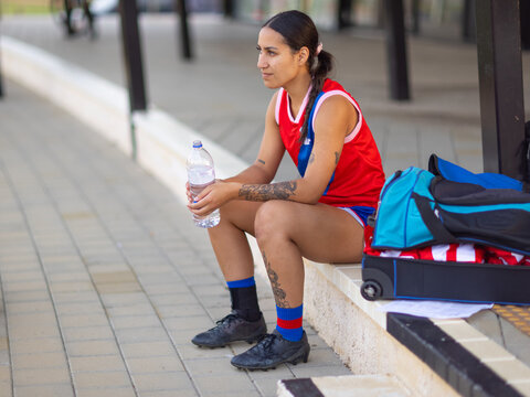 young female football player resting on step with water bottle