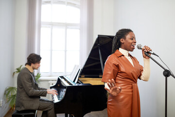 African woman in elegant leather dress standing and singing a song to microphone with composer...