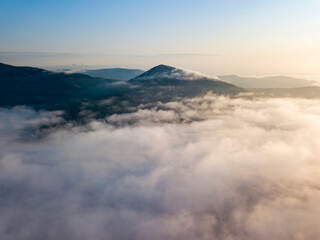 Flight over fog in Ukrainian Carpathians in summer. Mountains on the horizon. Aerial drone view.